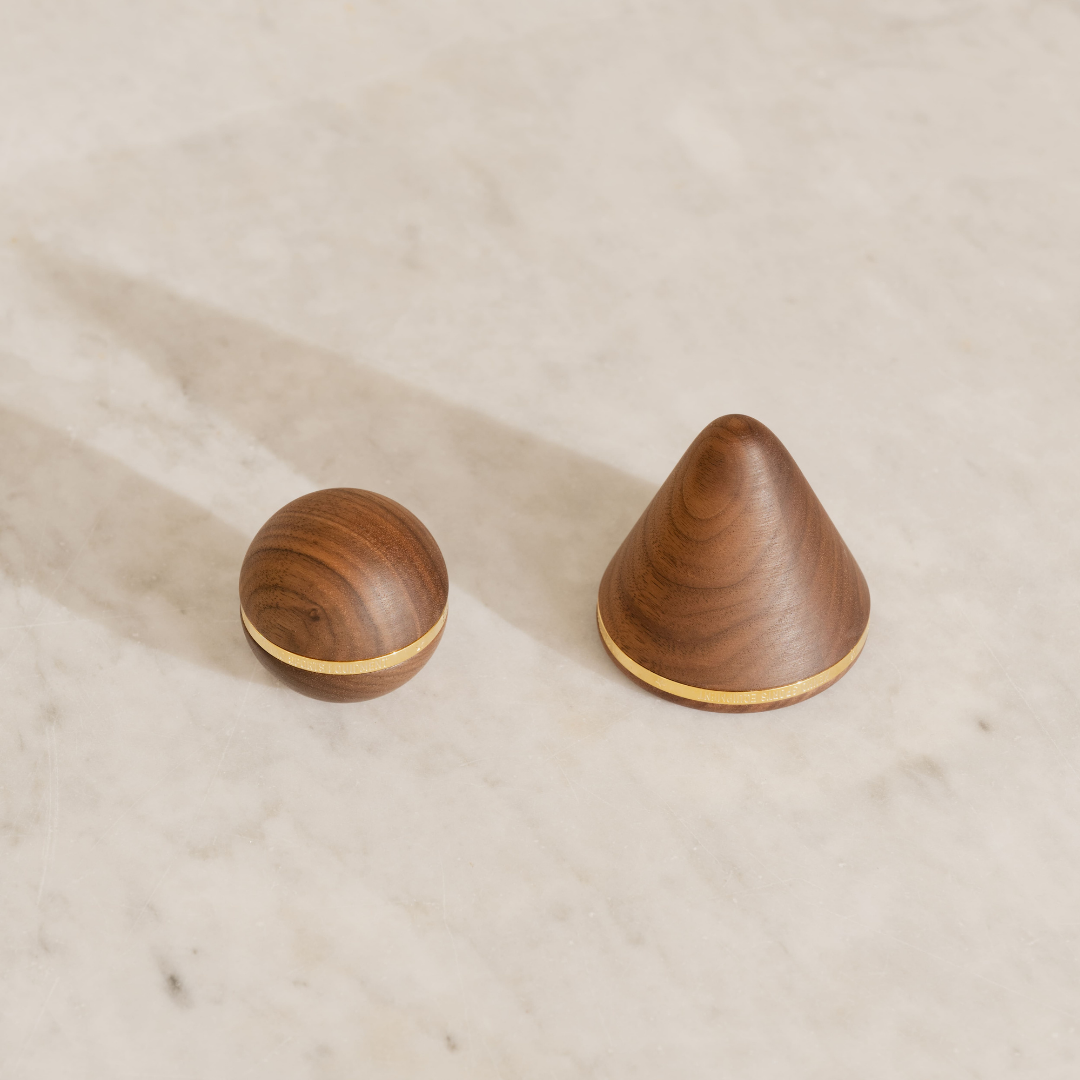 Walnut ball and cone with gold bases on a beige surface