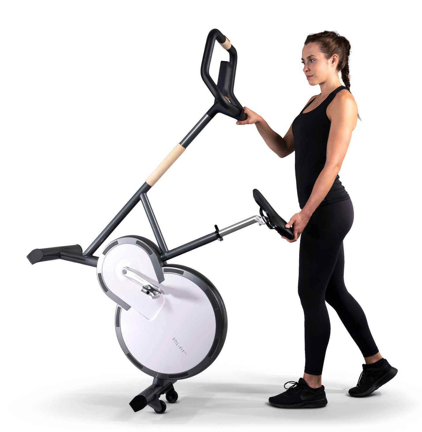 A fitness instructor holding a stylish modern exercise bike with a sleek design, featuring three adjustable grip positions and a multifunctional console. Stil-Fit Ergometer Pure - Stationary Bike