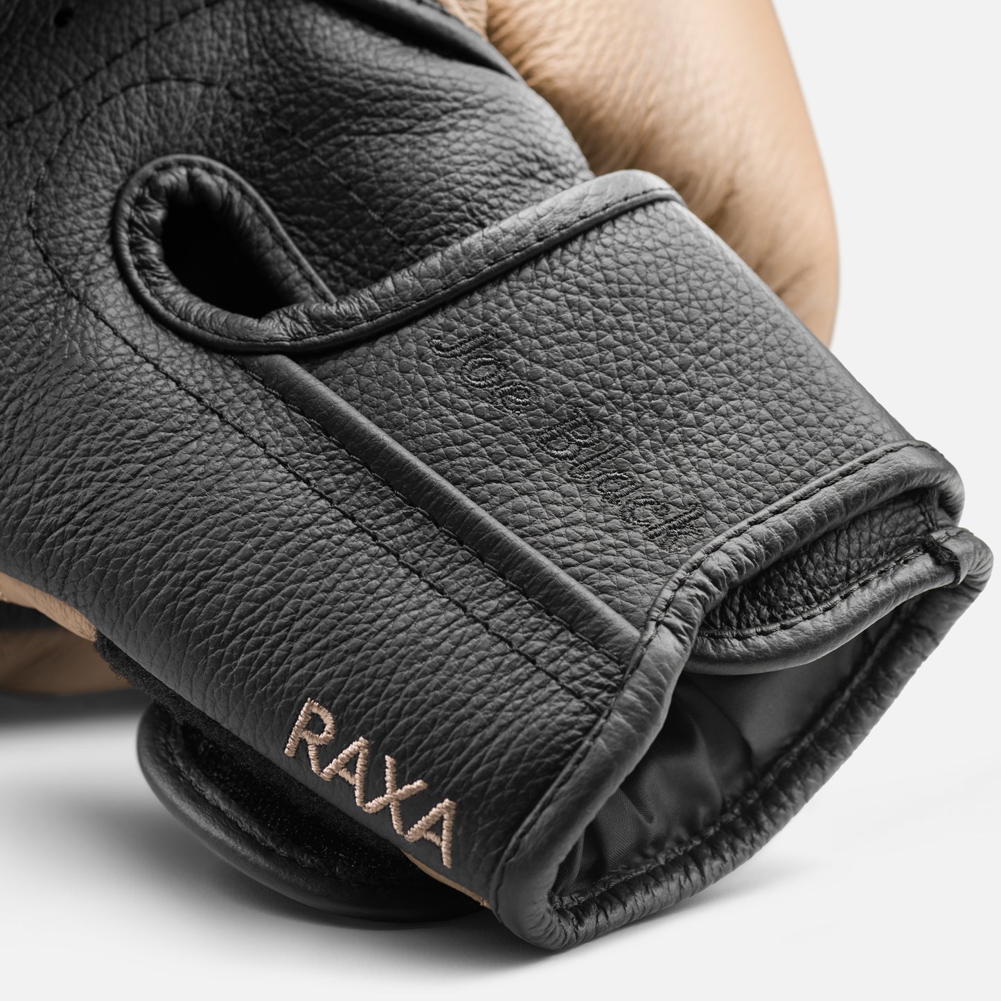 Details image of the hand-stitched initials on the leather for luxury fitness equipment, handmade boxing gloves with premium Italian leather, with default color for base & accent leather. PENT. RAXA - Luxury Boxing Gloves