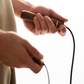Close-up of hands holding a walnut skipping rope on a plain background