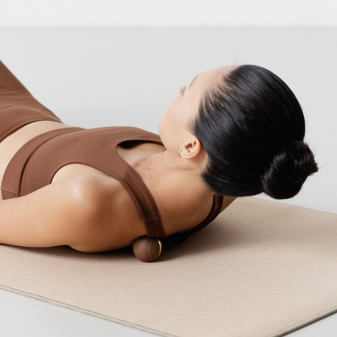 Woman using a kenko massage roller on a mat with a neutral background