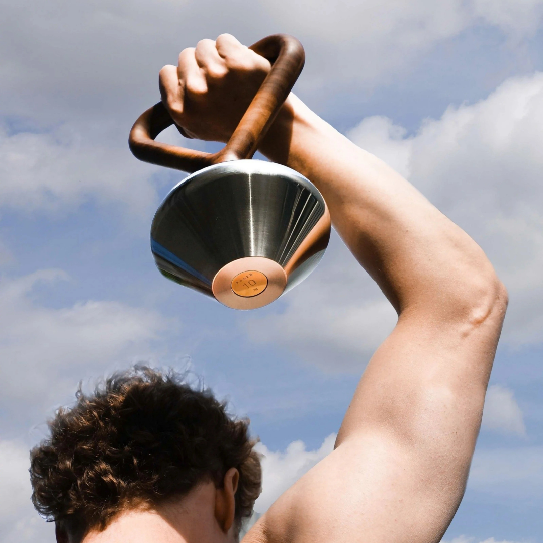 Luxury kettlebell combining solid wood grip, polished stainless steel body, and gold-plated accents.