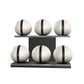 Six white leather medicine balls with black accent leather, arranged on two shelves made of black ash wood. PENT. MOXA Set Ultimate - Set of 6 Medicine Balls on Horizontal Wooden Stand