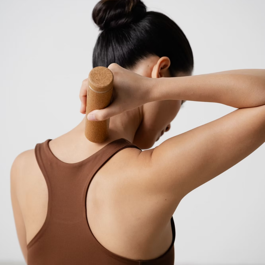 Woman using a cork stick on her neck against a plain background