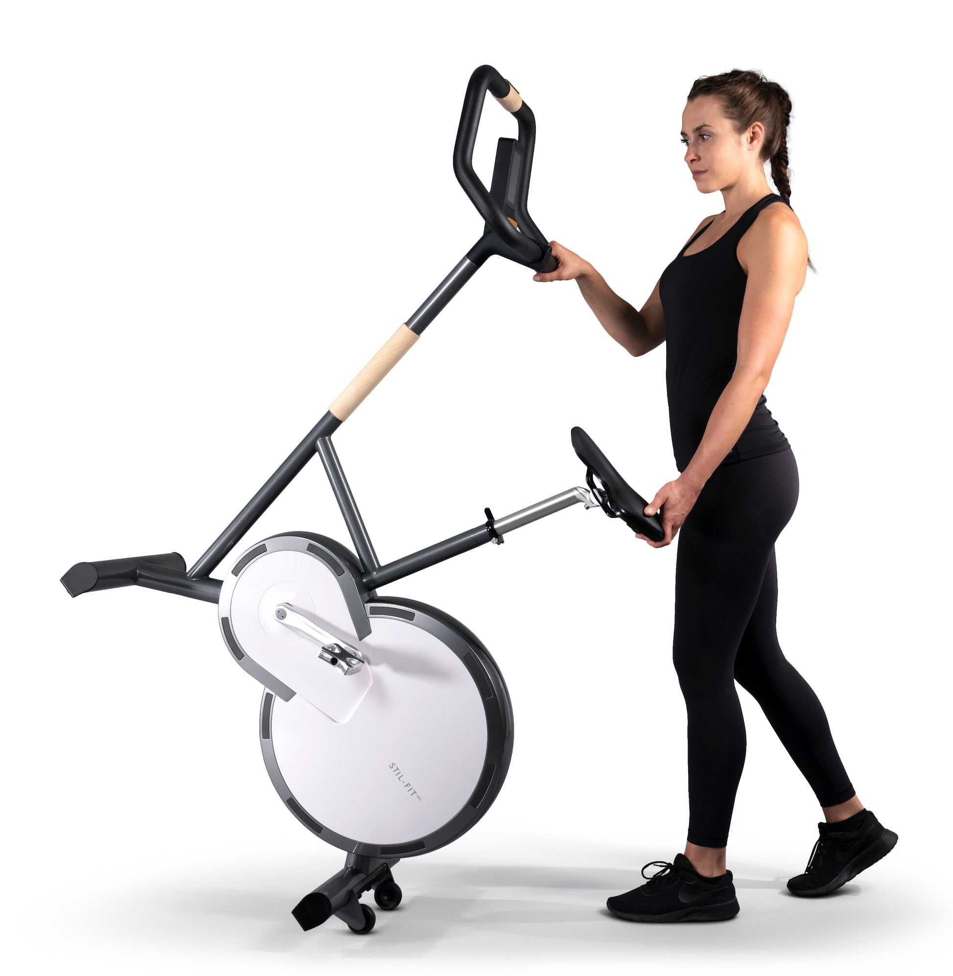 A fitness instructor holding a stylish modern exercise bike with a sleek design, featuring three adjustable grip positions and a multifunctional console. Stil-Fit Ergometer Pure - Stationary Bike