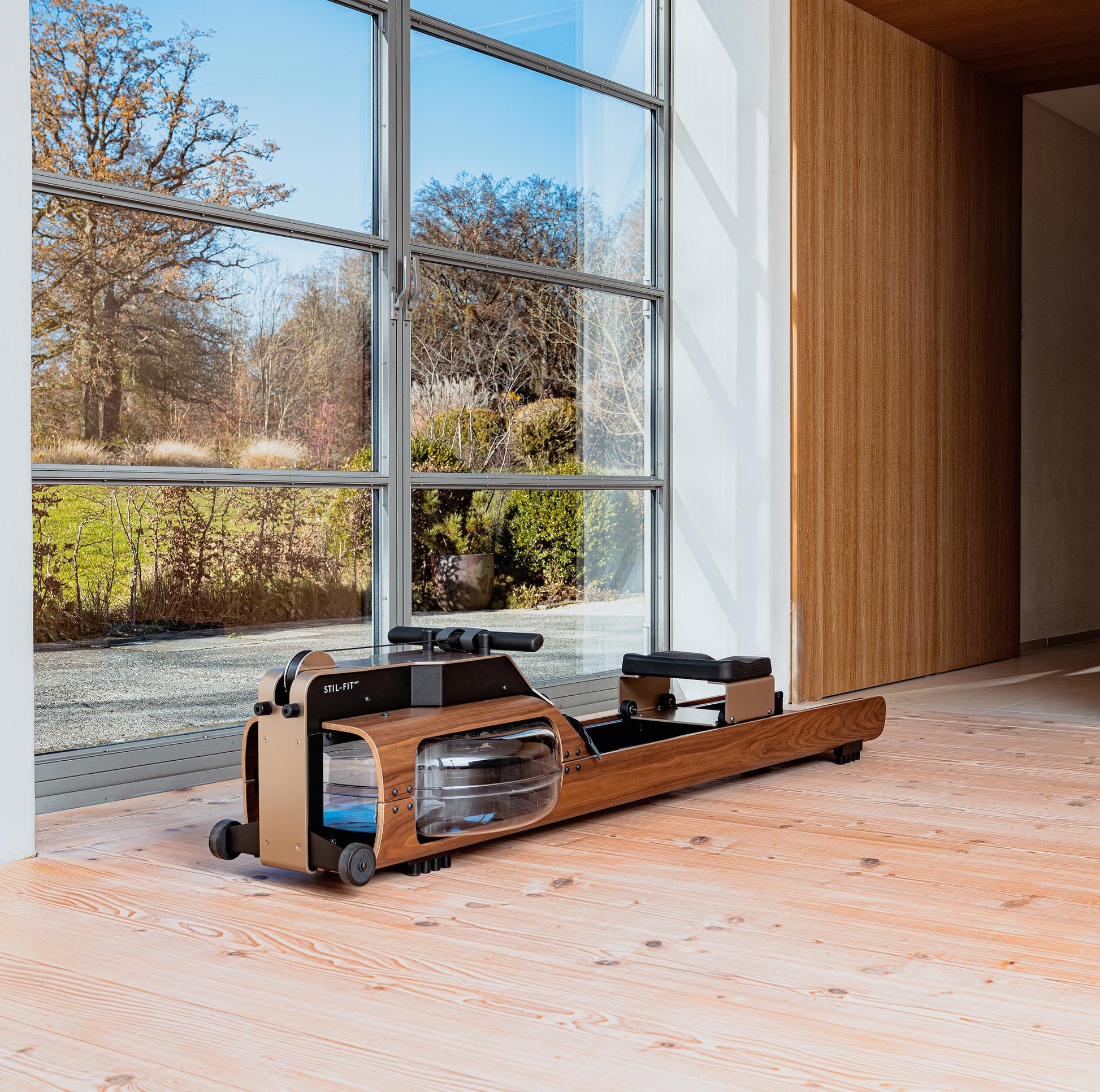 A luxury fitness equipment, walnut wooden water rowing machine placed in luxury home gym, for full-body workout with the soothing sounds of water. Stil-Fit Flow One - Rowing Machine with water resistance